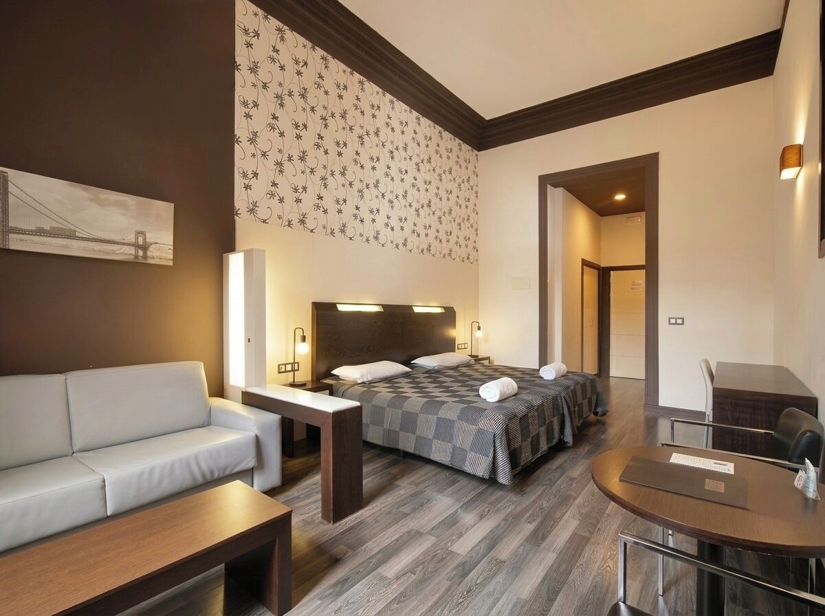 A hotel room with a bed, a sofa, a desk, and a chair.