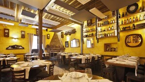 Un restaurant doté de nombreuses tables, prêt à accueillir les clients, avec une variété de bouteilles de vin exposées sur des étagères et une cheminée en pierre rustique.