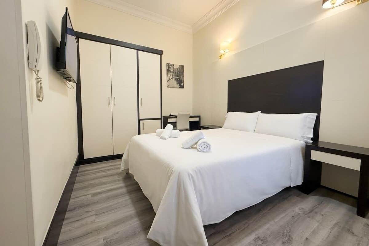 Una habitación de hotel con cama, mesita de noche, armario y un tocador.