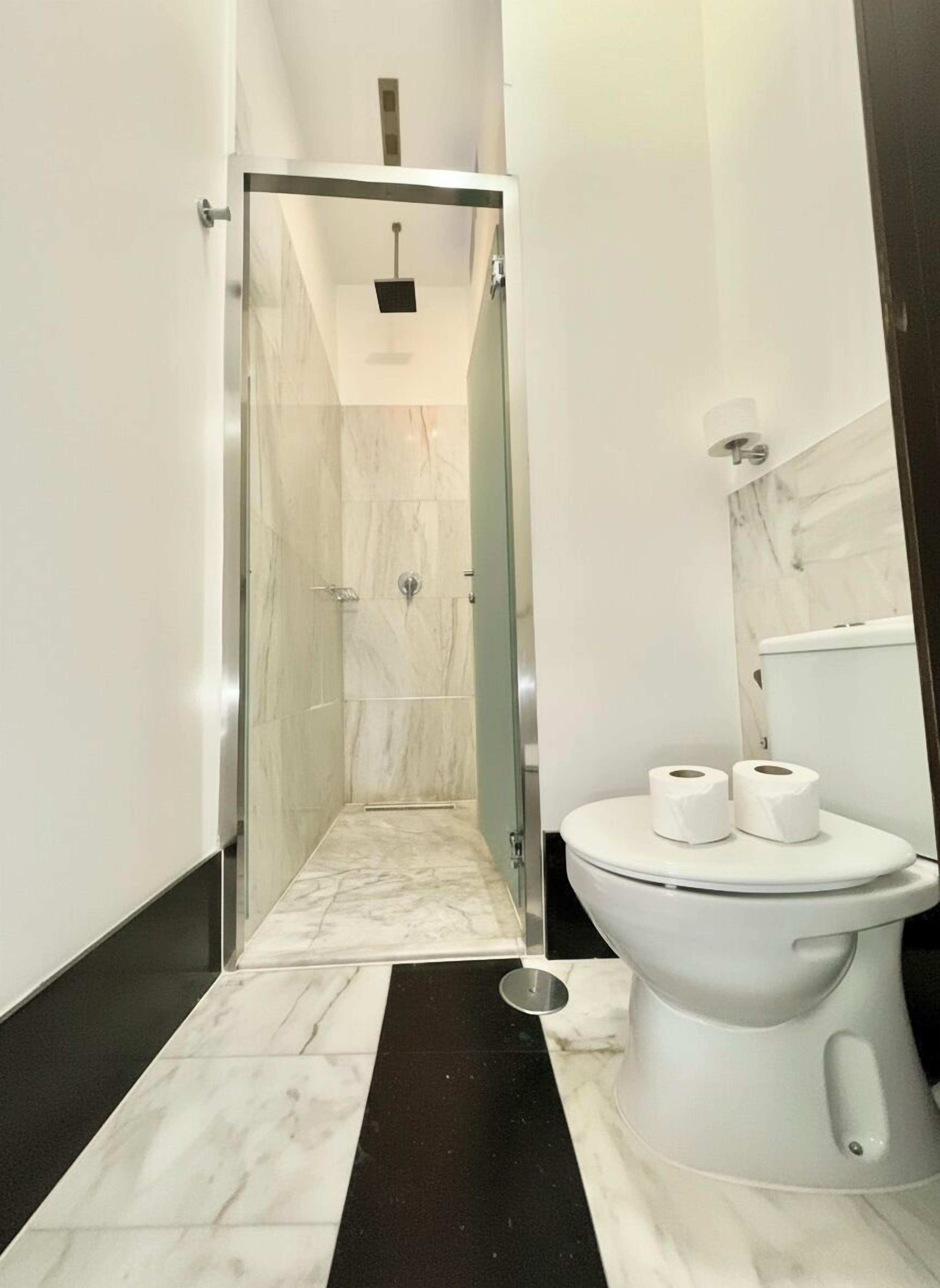 A modern bathroom with a glass-enclosed shower, a toilet with two rolls of toilet paper, and a marble floor.