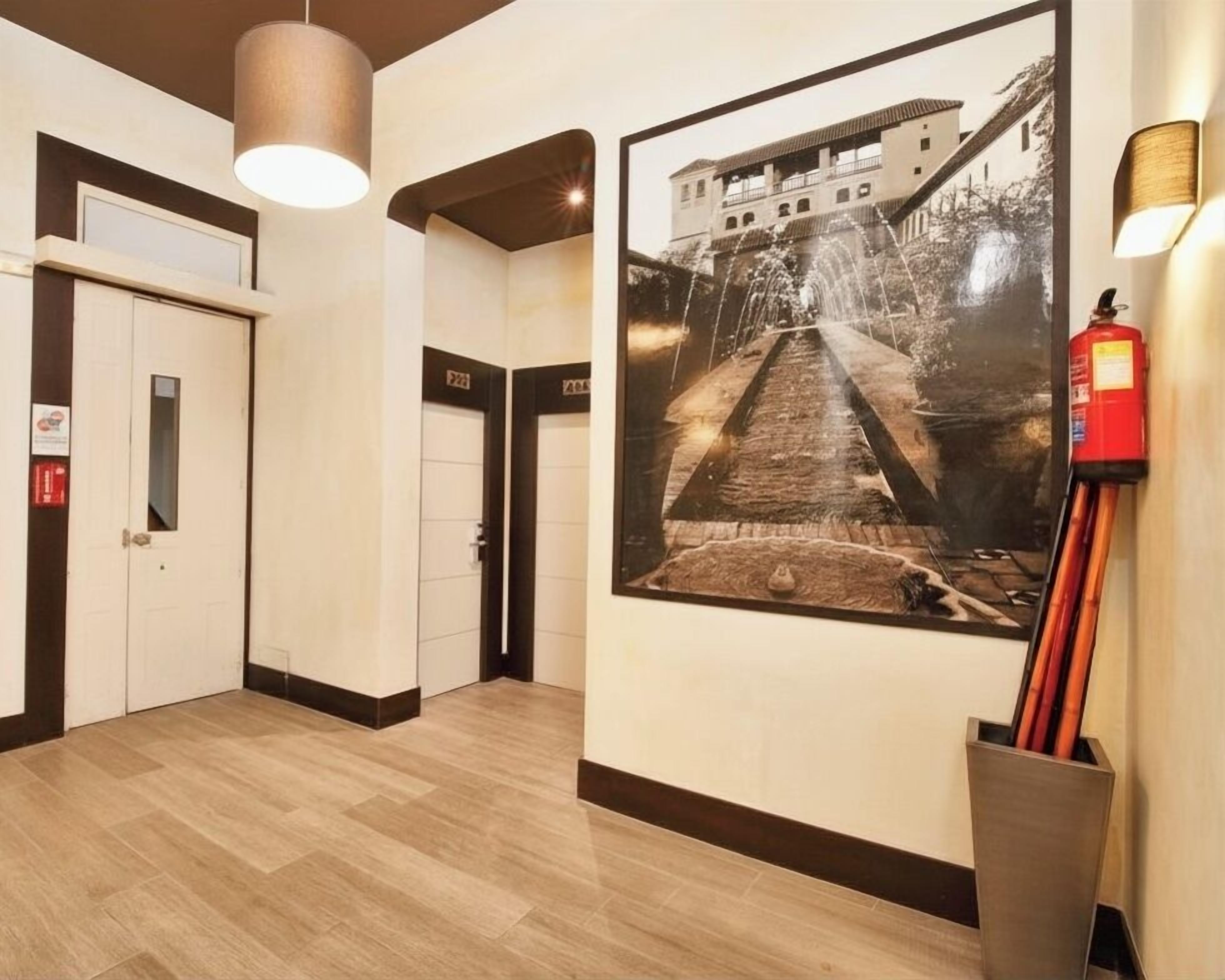 A hallway with a framed photograph of a building, a fire extinguisher, and a door.