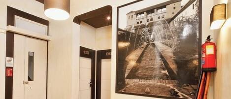 A hallway with a framed photograph of a building, a fire extinguisher, and a door.