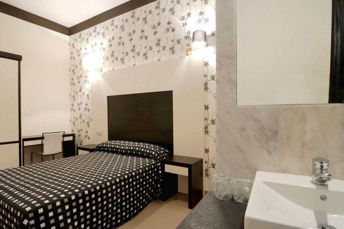 Una habitación de hotel con cama, mesita de noche y baño con lavabo y espejo.