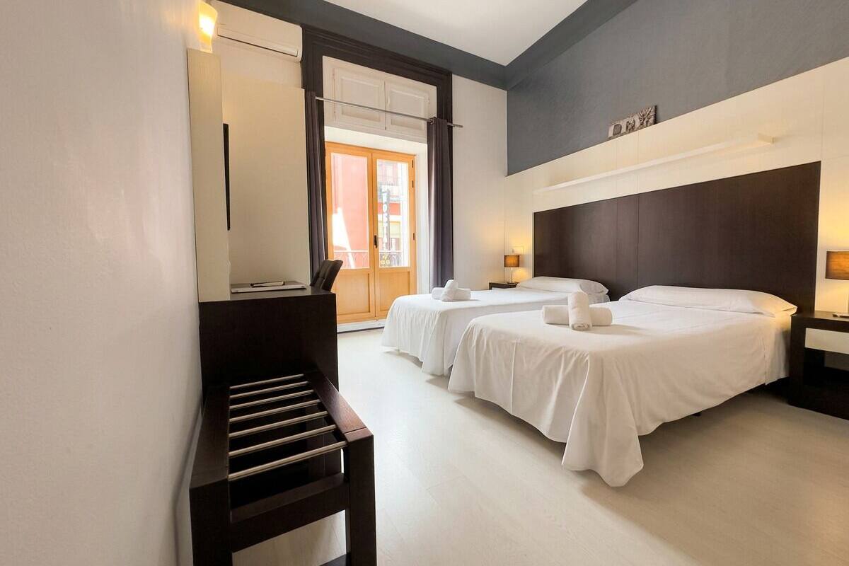 Habitación de hotel con dos camas, un escritorio y un ventanal grande.