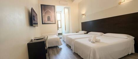 A hotel room with three beds, a desk, a chair, a chandelier, and a painting on the wall.