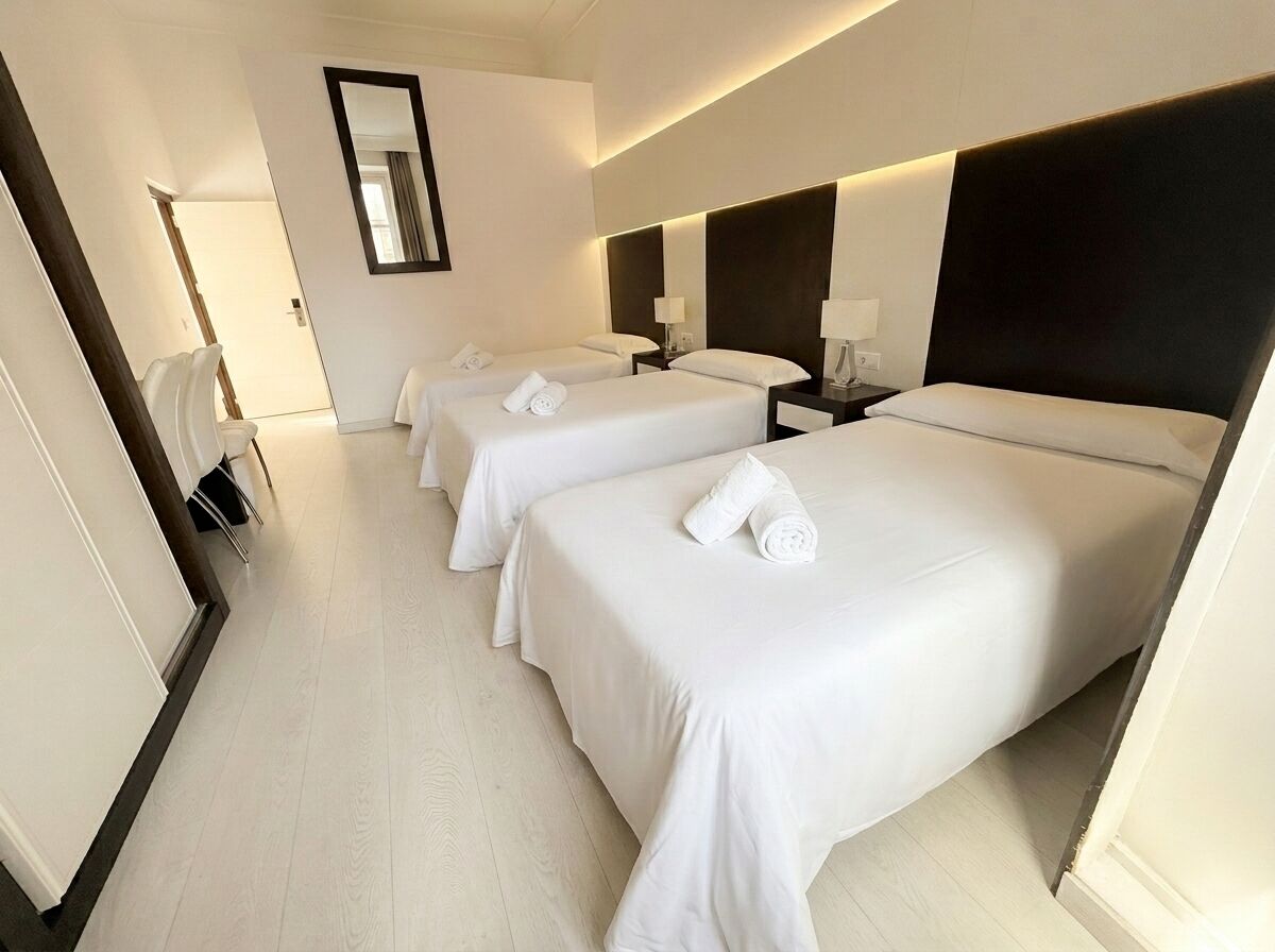 A hotel room with three beds, a large mirror, and a modern design.