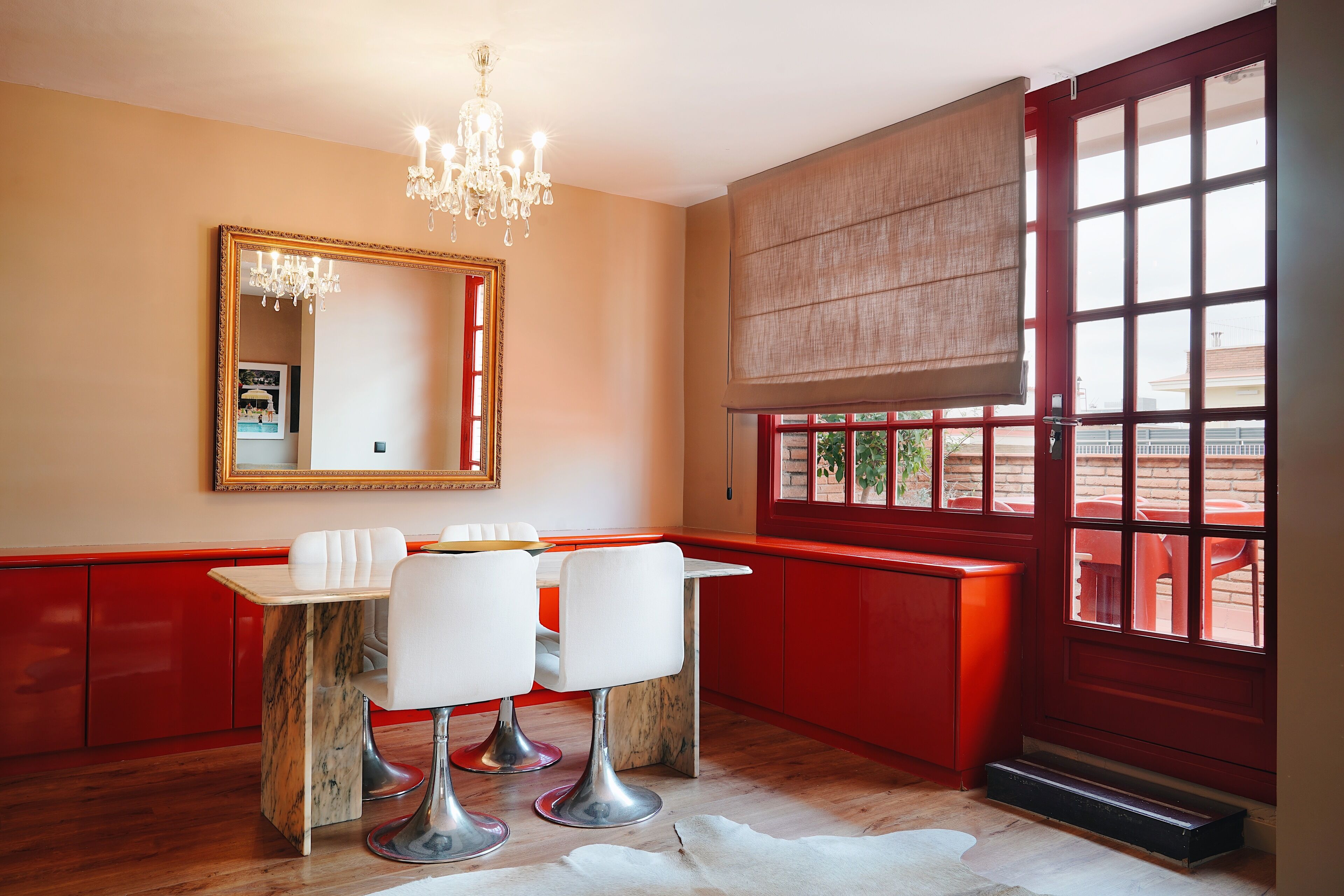 Una habitación con una decoración en tonos rojos y beige, un candelabro, un espejo grande y una ventana con vistas a un área de estar al aire libre.