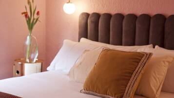 A neatly made bed with white and brown pillows, a clear vase with flowers, and a wall-mounted light fixture.