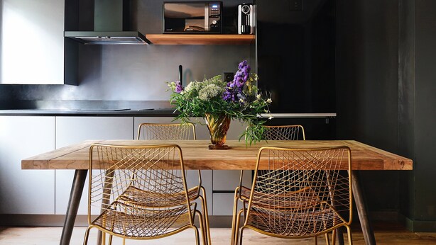 A dining area with a wooden table, four wireframe chairs, and a vase with flowers. - Isabella's House (Barcelona)