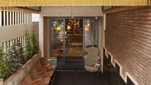 A hotel entrance with a brick wall, a wooden bench outside, and a view into the interior featuring a sofa and a lamp. - Isabella's House (Barcelona)