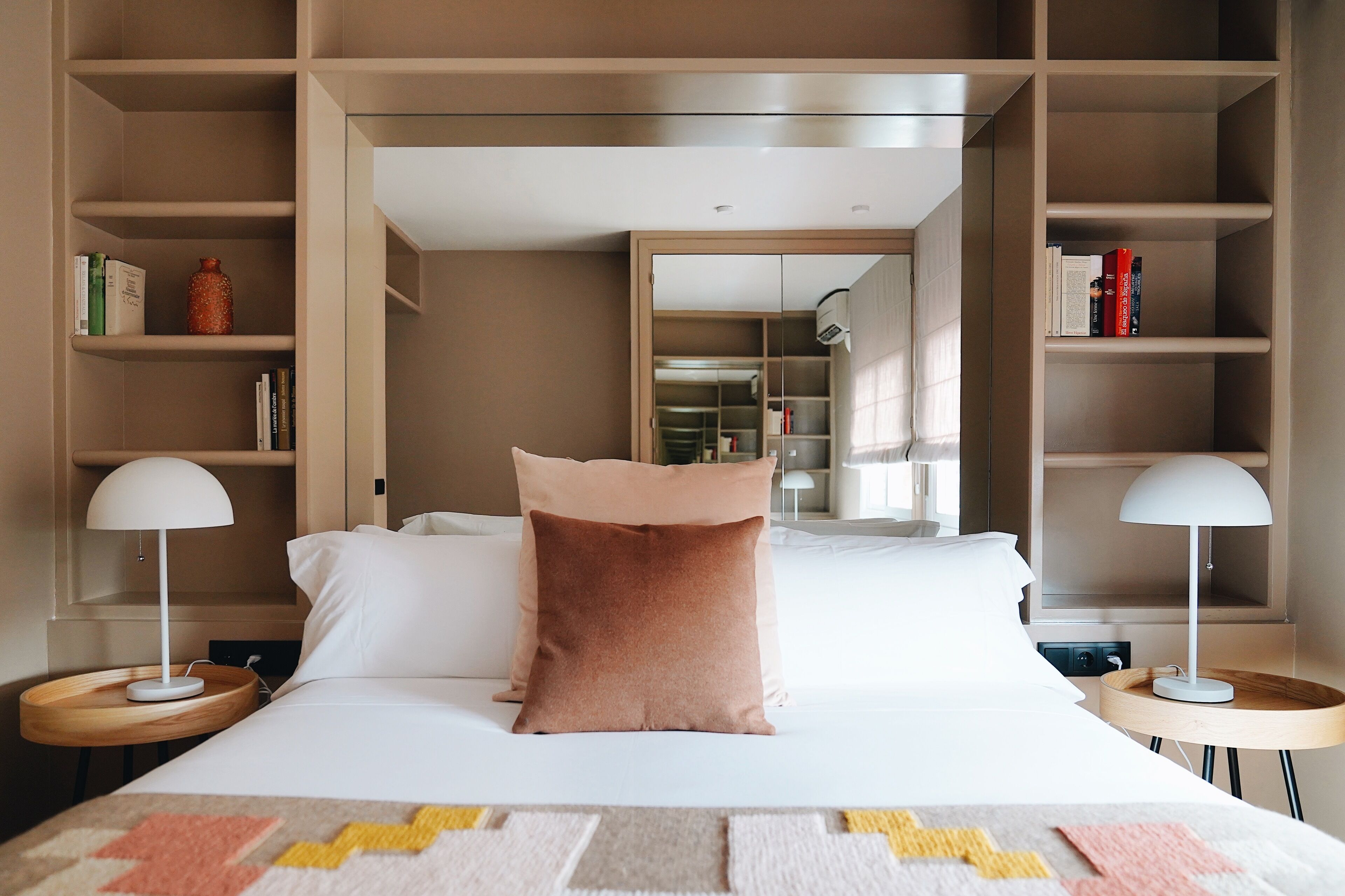 A neatly arranged hotel room with a large bed, two bedside tables with lamps, a bookshelf, and a wardrobe.