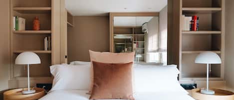 A neatly arranged hotel room with a large bed, two bedside tables with lamps, a bookshelf, and a wardrobe.