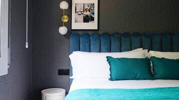 Un lit bien fait, avec une literie blanche et turquoise, un mur foncé à la texture intéressante et une photo encadrée au-dessus du lit.
