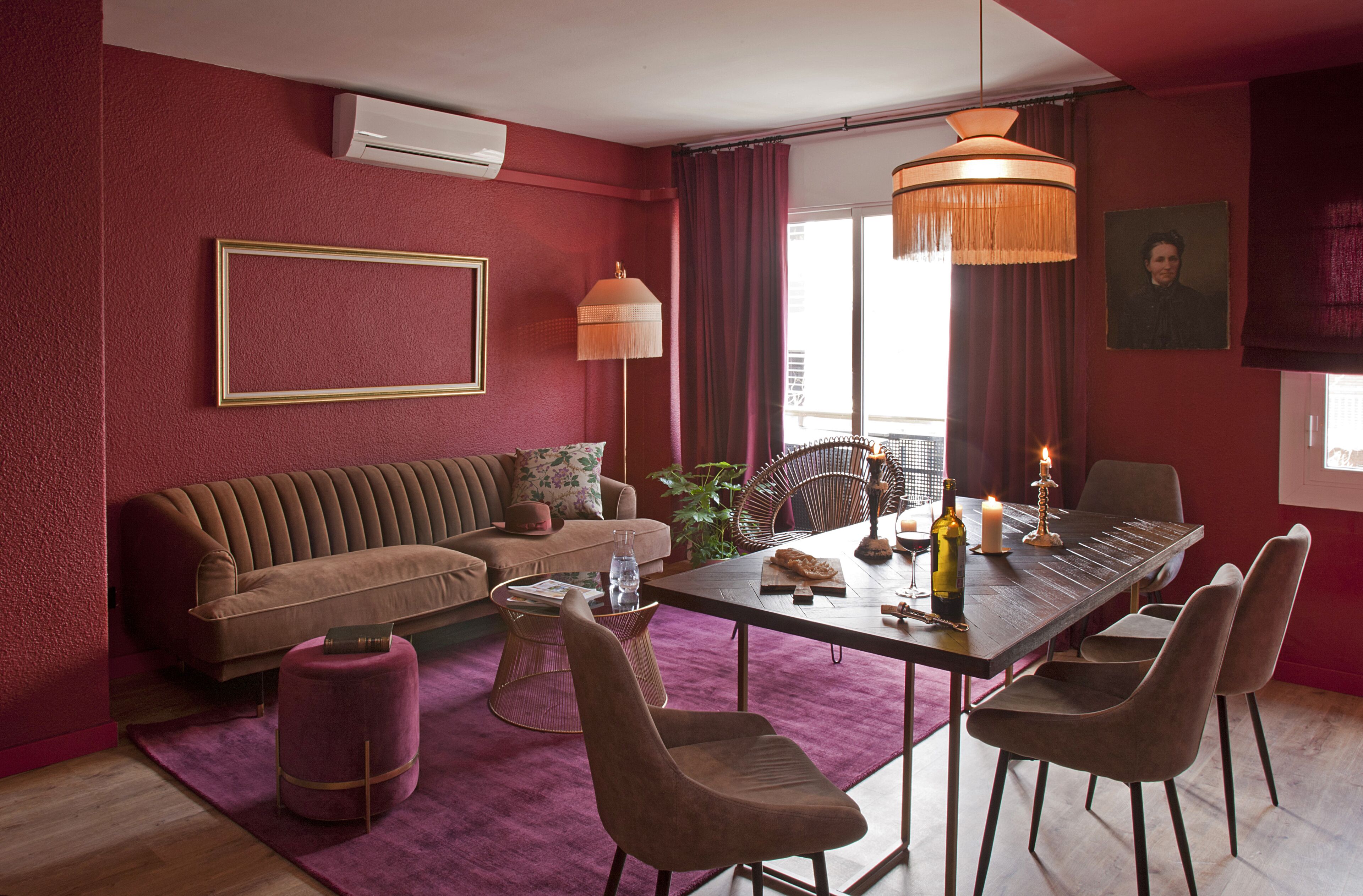 A modern living room with a brown sofa, a dining table with chairs, a pendant light, and a large window with curtains.