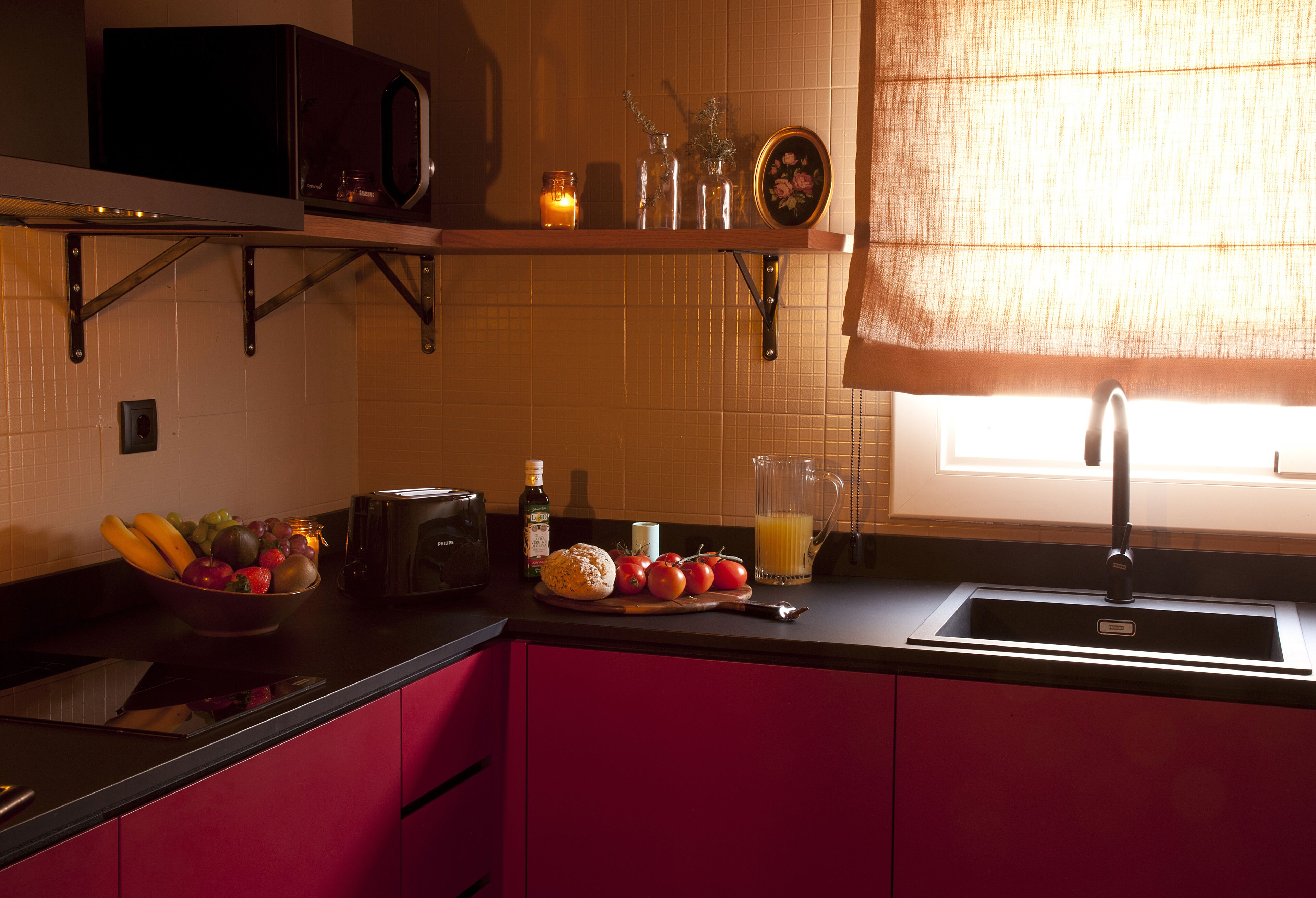 Eine Küche mit Mikrowelle, Toaster und Spüle. Auf der Arbeitsfläche liegen Früchte, eine Flasche und ein Glasbehälter.