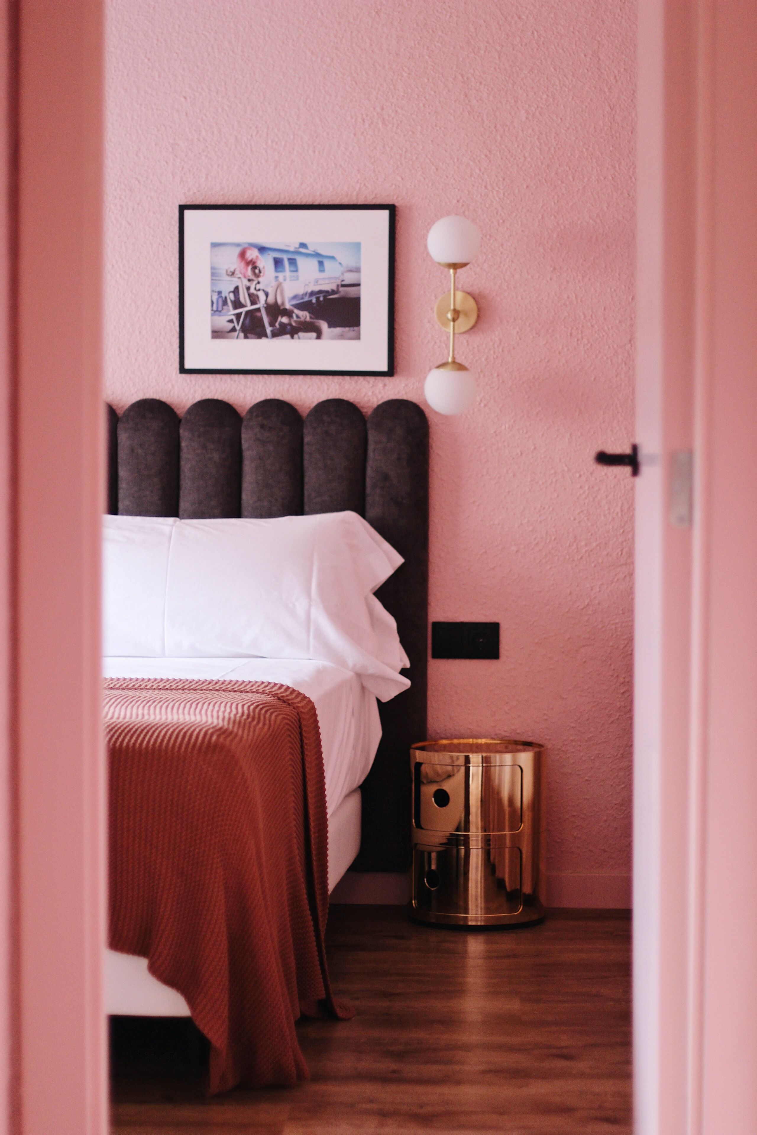 Un dormitorio con una cama, un cuadro en la pared, una lámpara de noche y un cubo de basura.