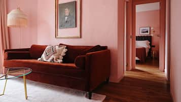 A room with a red velvet sofa, a glass coffee table, a framed portrait on the wall, and a bed in the background.