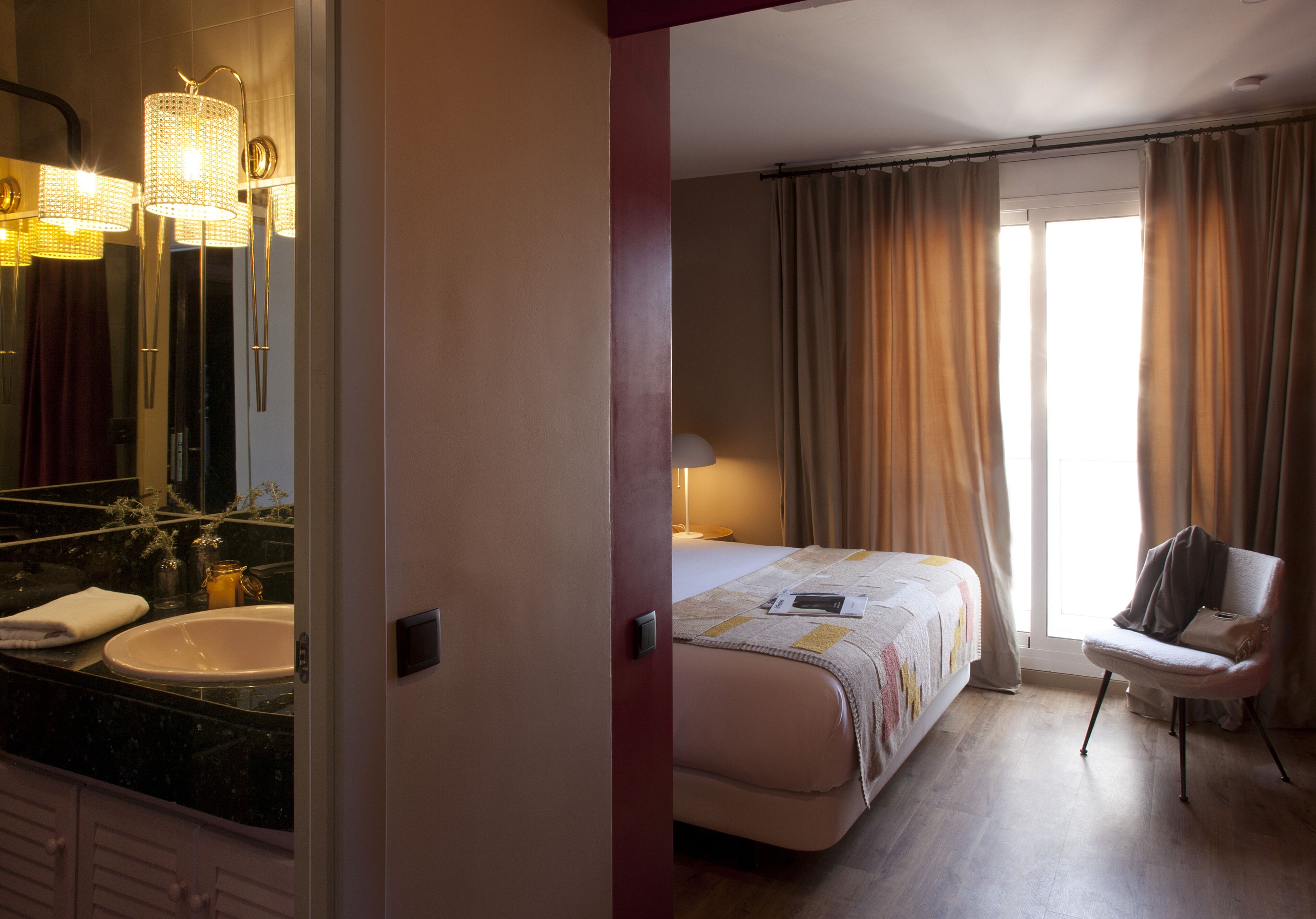 Una habitación de hotel con un espejo grande, una cama, una silla y una ventana con cortinas.