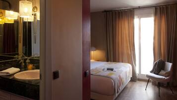 Una habitación de hotel con un espejo grande, una cama, una silla y una ventana con cortinas.