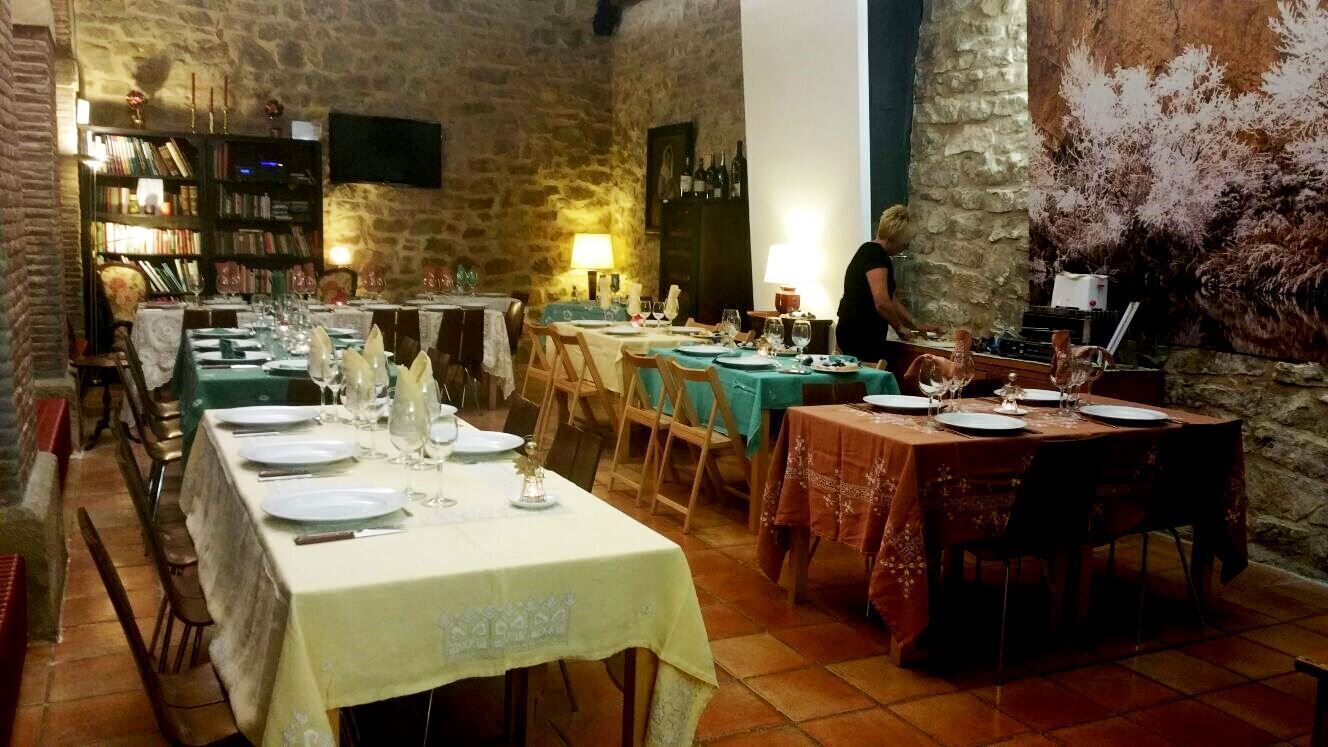 A restaurant with stone walls, multiple tables set for dining, and a bookshelf in the background.