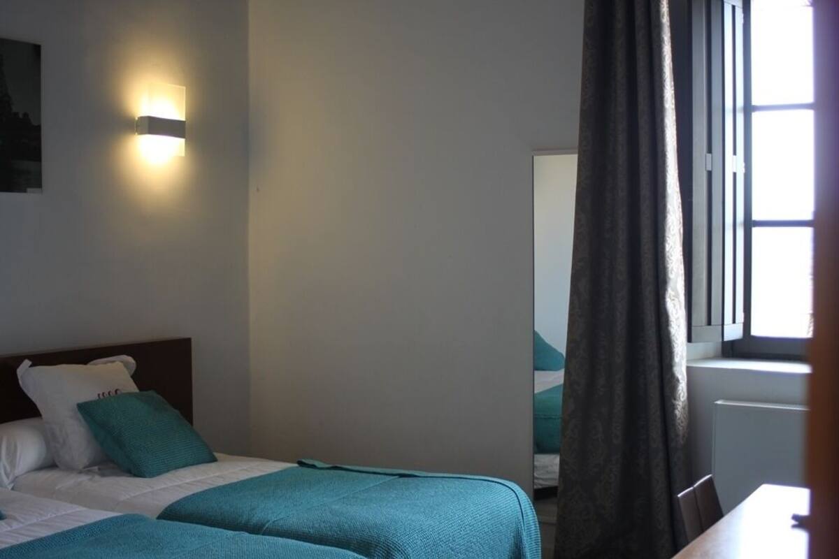 Ein Hotelzimmer mit zwei Betten, einem Nachttisch, einer Wandleuchte und einem Fenster mit Vorhängen.