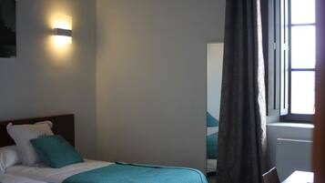 Een hotelkamer met twee bedden, een nachtkastje, een wandlamp en een raam met gordijnen.