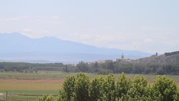 Paisaje rural con una cadena montañosa al fondo, cielo despejado y algunos edificios en una colina.