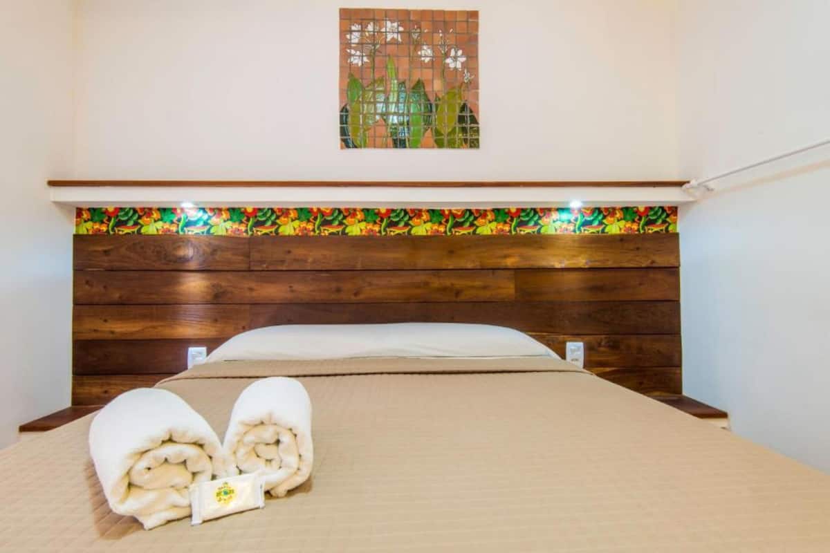 Quarto de hotel com cabeceira de madeira, painel de azulejos coloridos e cama bem arrumada com toalhas.