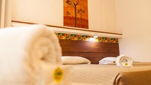 A hotel room with a wooden headboard, a bed with white linens, and a painting of a tree on the wall. - Pousada Bahia Brasil (Cairu)