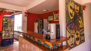 A bar area with a counter, a refrigerator, a coffee machine, and a colorful mural on the wall. - Pousada Bahia Brasil (Cairu)