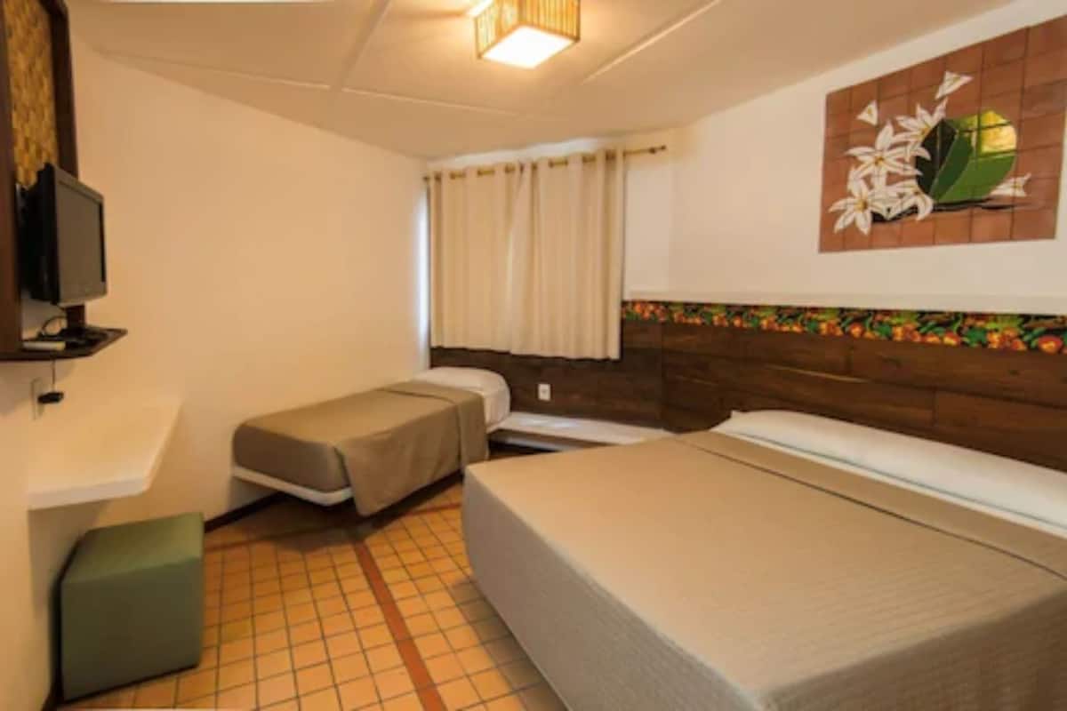 Quarto de hotel com uma cama, uma pequena escrivaninha e uma janela com cortinas.