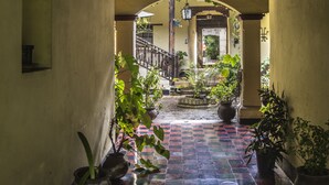 A corridor with tiled flooring, potted plants, and a wooden ceiling structure. - Hotel Museo Mayan Inn de Guatemala (Chichicastenango)