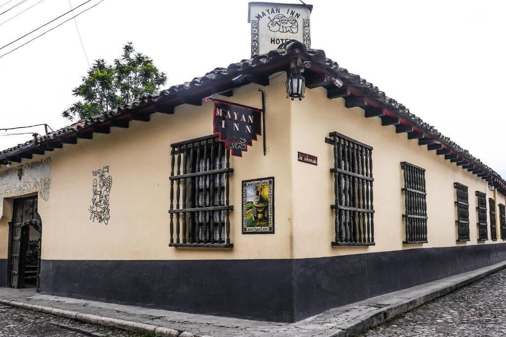 Un edificio con un cartello che riporta “Mayan Inn Hotel” e uno stile architettonico tradizionale, con tetto in tegole e finestre con grate.