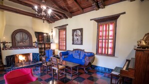 A traditional room with a fireplace, a red sofa, a blue sofa, a wooden table, and a piano. - Hotel Museo Mayan Inn de Guatemala (Chichicastenango)