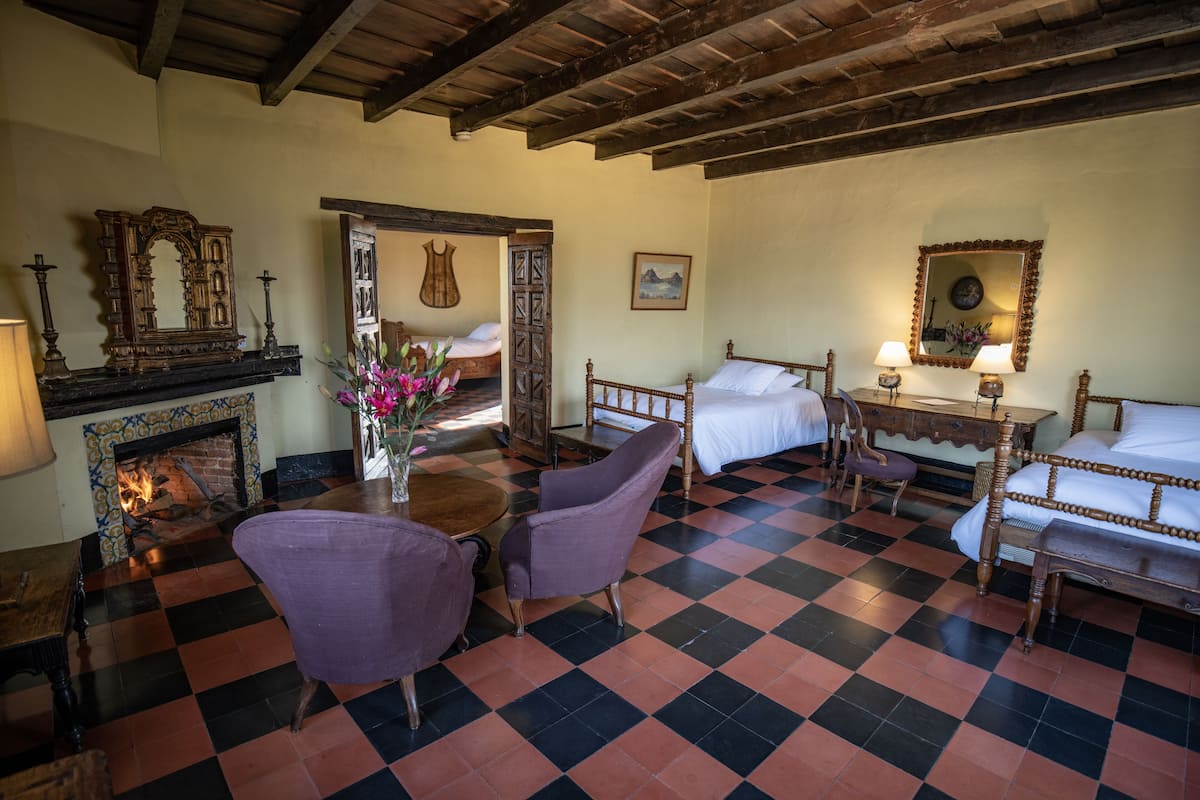 A room with a checkered floor, wooden furniture, a fireplace, and a bed with a wooden headboard.