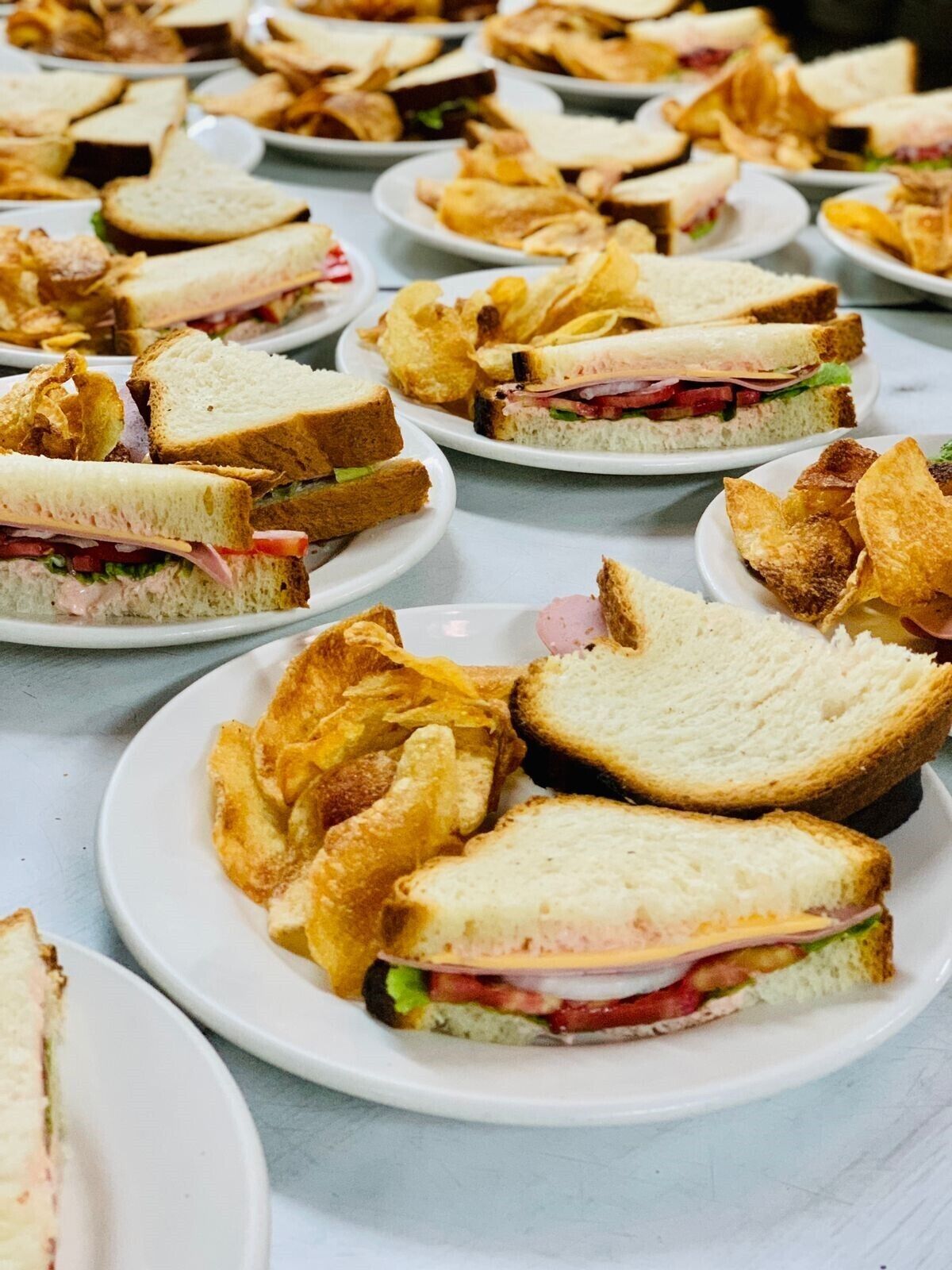 A table with plates of sandwiches and chips.