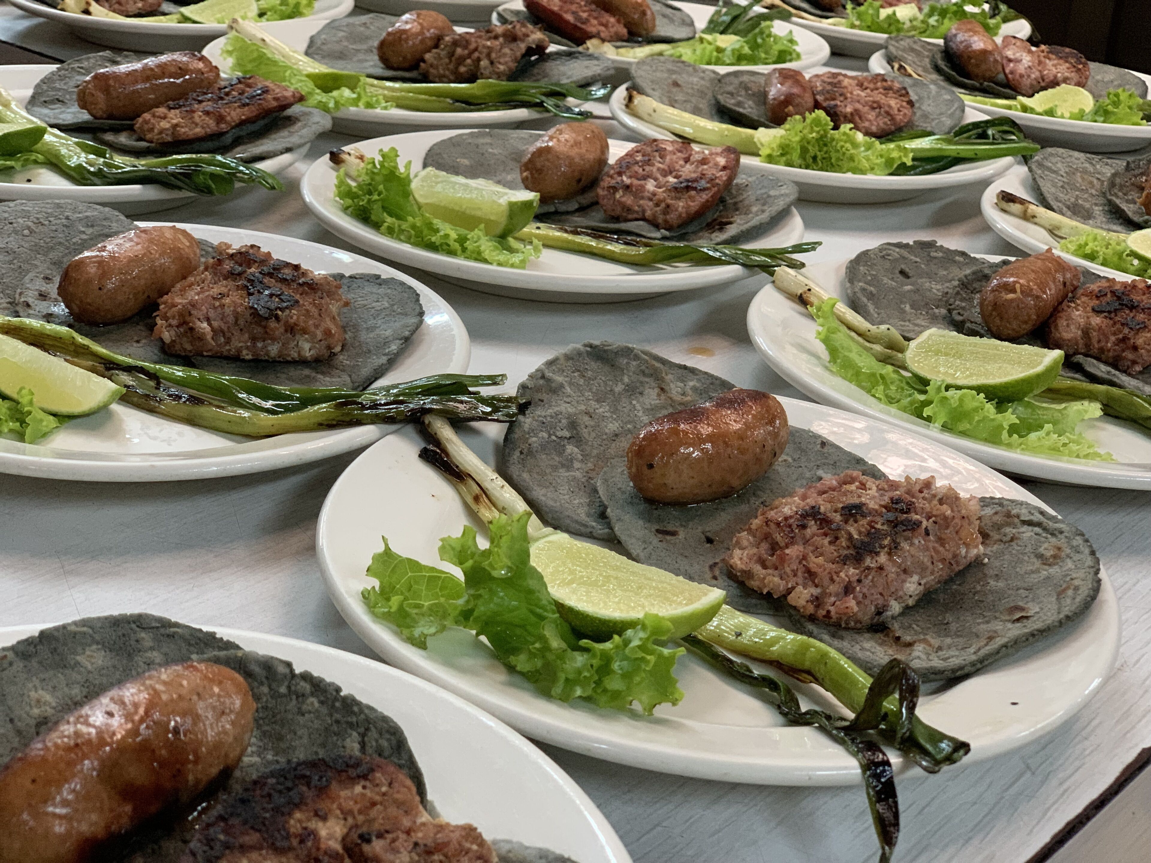 A table with multiple plates of food, each containing meat, lettuce, and lime slices.