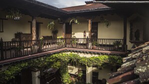 A courtyard with a wooden balcony, potted plants, and a tiled roof. - Hotel Museo Mayan Inn de Guatemala (Chichicastenango)
