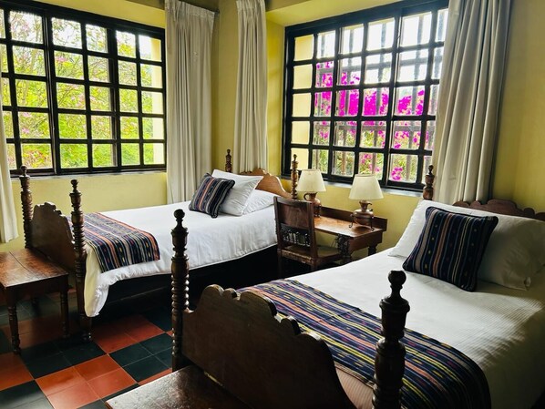 A room with two beds, a wooden chair, a nightstand, and a window with curtains. - Hotel Museo Mayan Inn de Guatemala (Chichicastenango)