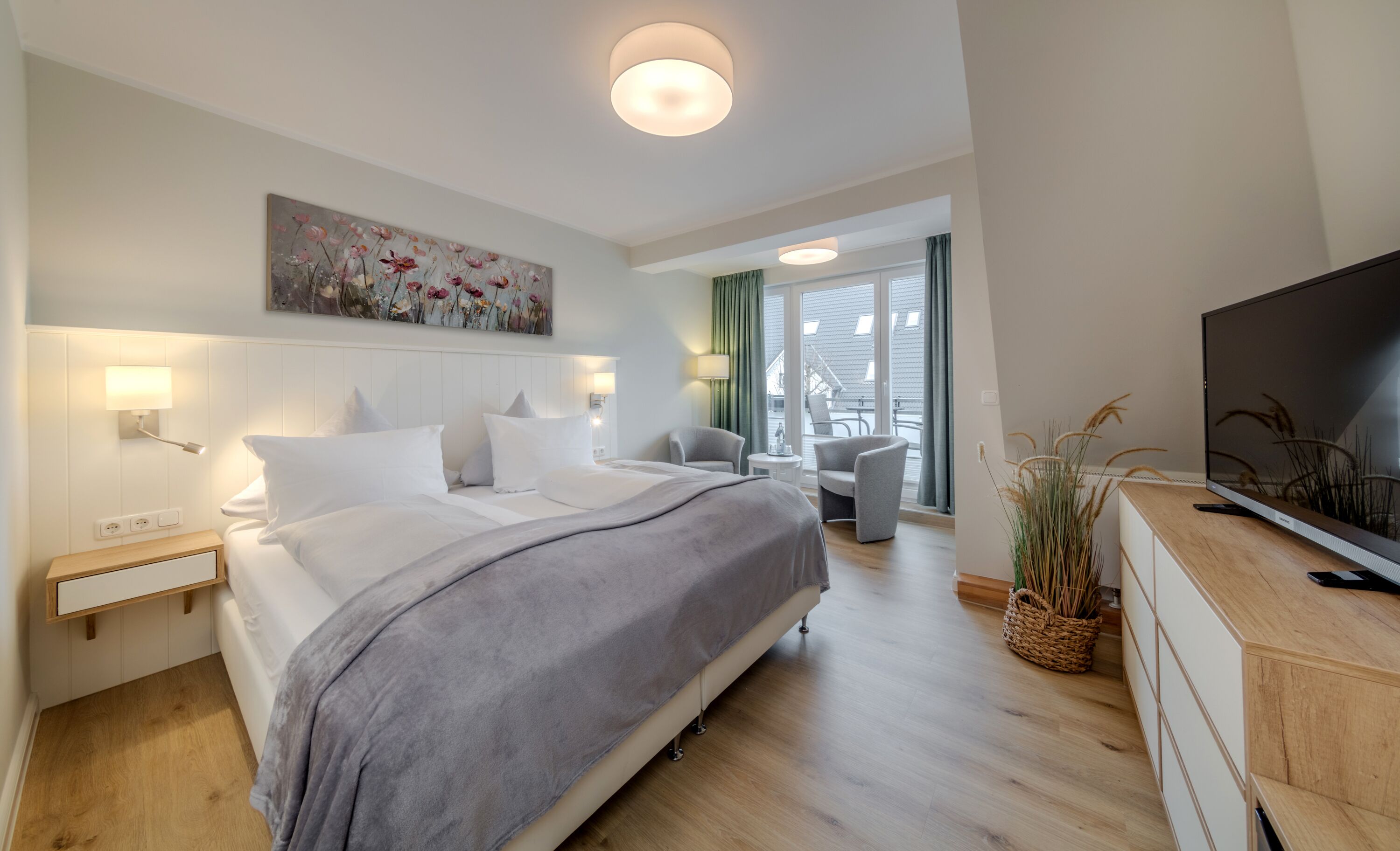 A modern hotel room with a large bed, bedside lamps, a flat-screen TV, a painting on the wall, and a view of the outdoors through the window.
