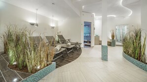 Un interior moderno con un área de descanso curvada, plantas en macetas y un espacio luminoso y bien iluminado con una puerta visible que conduce a otra habitación.
