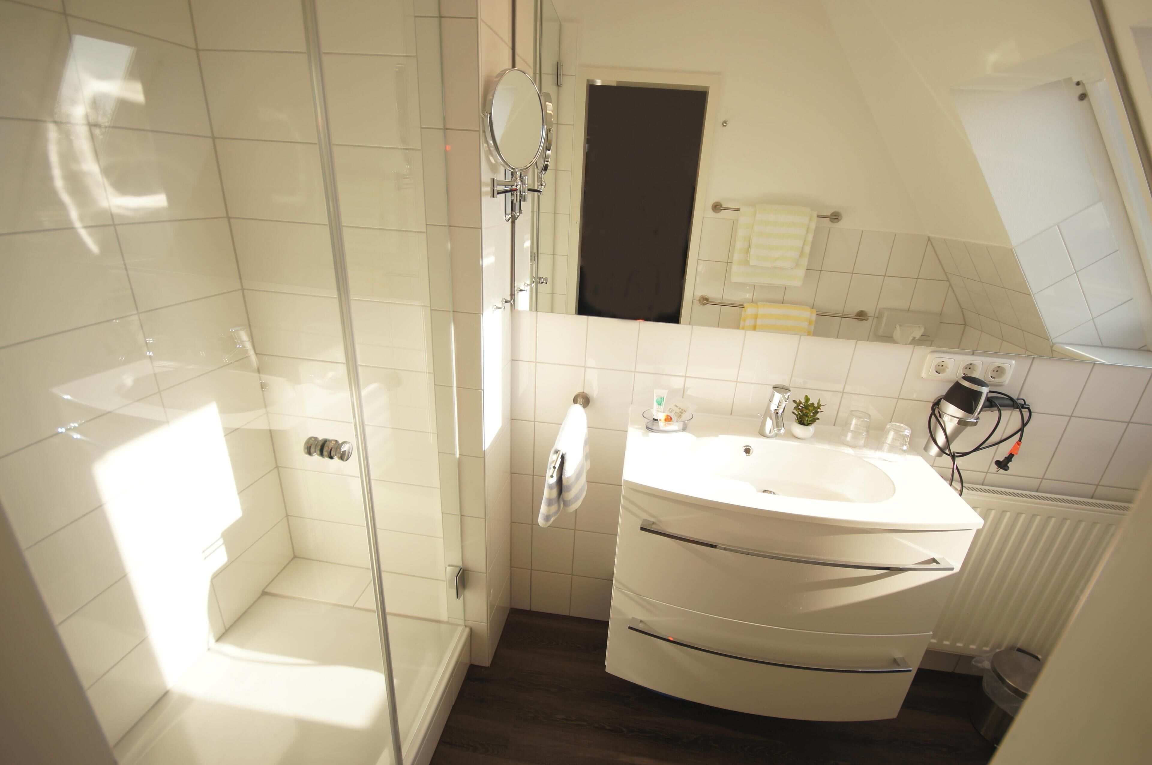 A modern bathroom with a glass-enclosed shower, a white sink with a mirror, and a towel rack.