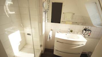 Un baño moderno con ducha envuelta en vidrio, un lavamanos blanco con espejo y un perchero para toallas.