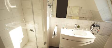 A modern bathroom with a glass-enclosed shower, a white sink with a mirror, and a towel rack.