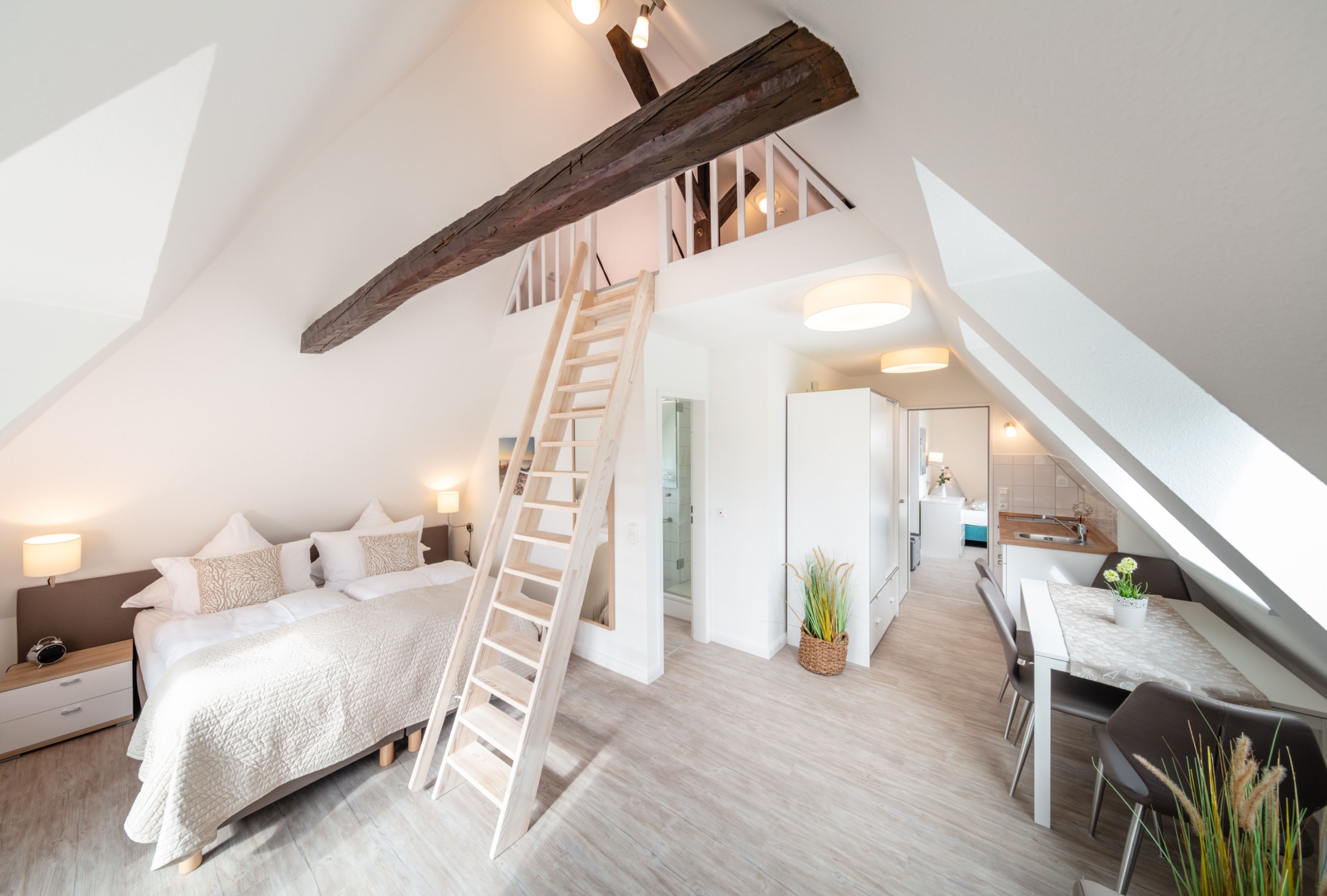 Ein modernes Loft-Schlafzimmer mit einer Holzleiter, die zu einer Erkerzone führt, einem gemütlichen Bett, einem Essbereich und einer Küche.
