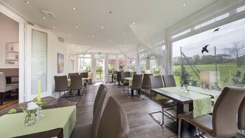 A spacious indoor dining area with tables and chairs, large windows, and a view of the outdoors.