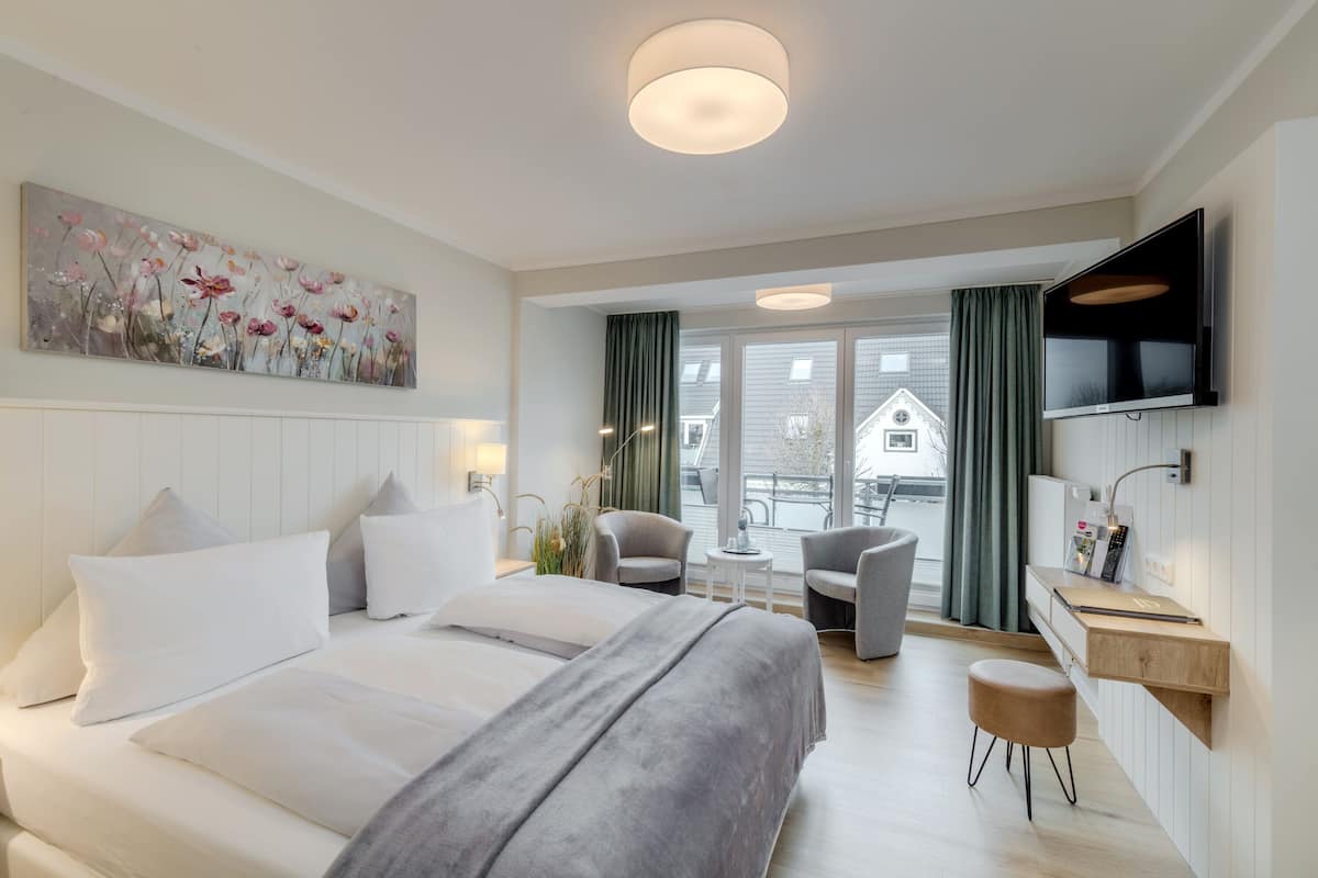 A modern hotel room with a large bed, a desk, a chair, and a TV.