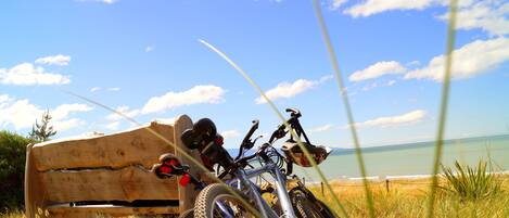 A wooden bench with a bicycle and helmet placed on it, overlooking a beach with clear skies.