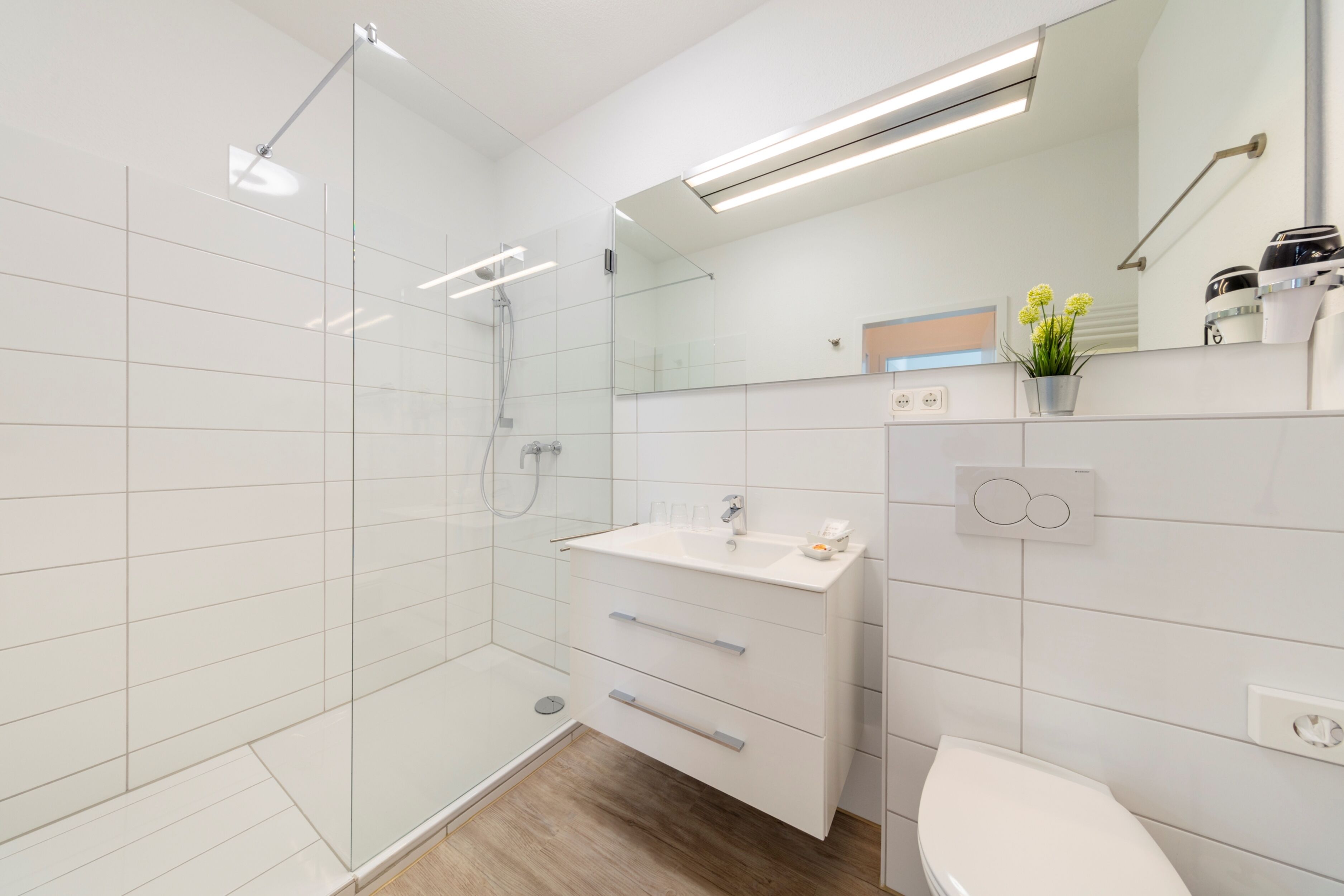 A modern bathroom with a glass shower enclosure, a white sink with a mirror above, and a toilet.