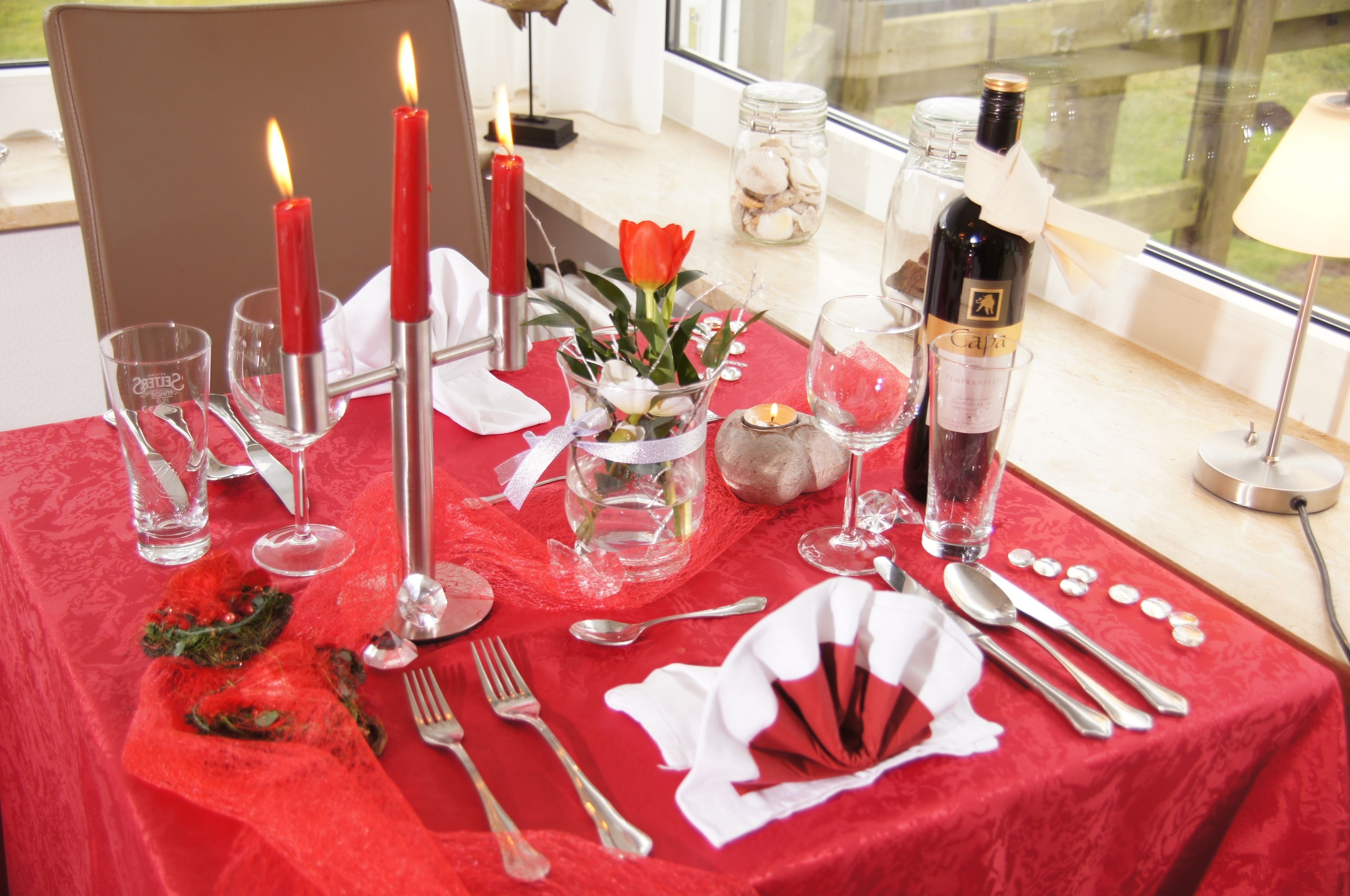 Une table mise pour un repas, avec des bougies, une bouteille de vin et un vase rempli de fleurs.